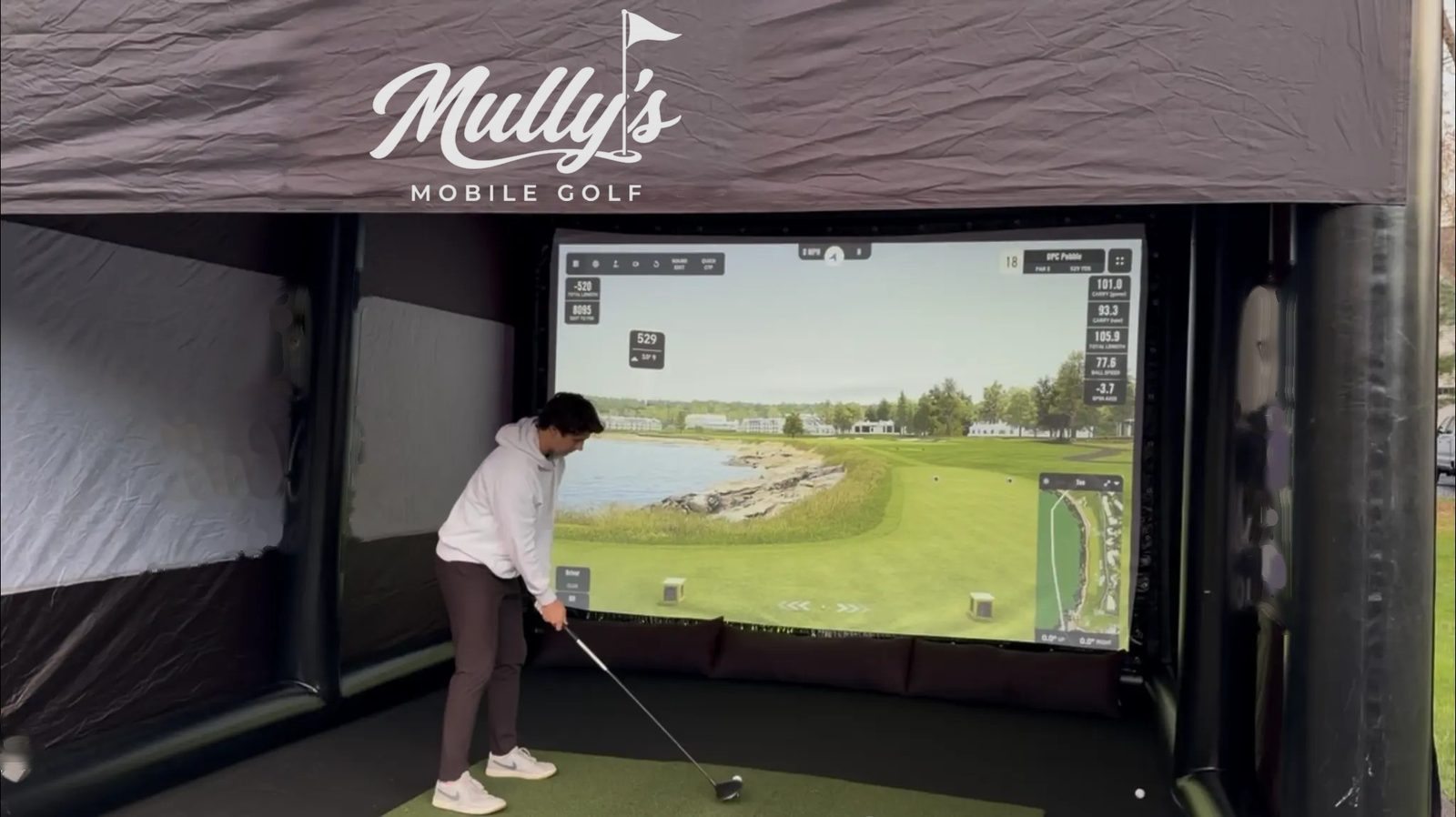 A golfer addressing the ball inside the simulator, the course on screen ahead